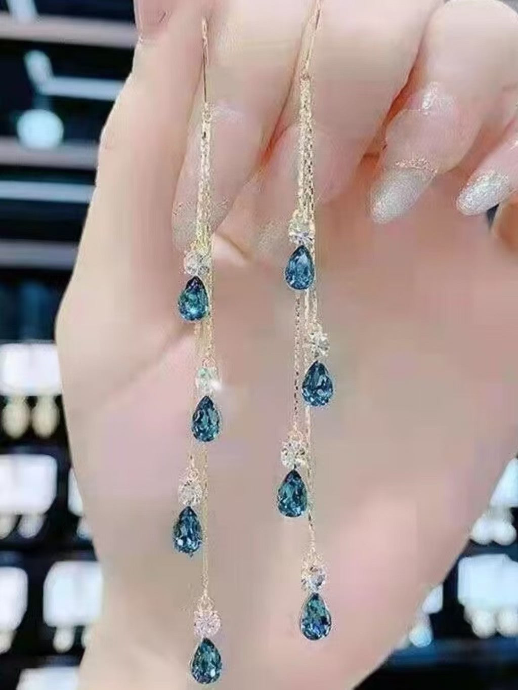 Blue crystal tassel ear line earrings with multi-teardrop gems, held in hand at retail store
