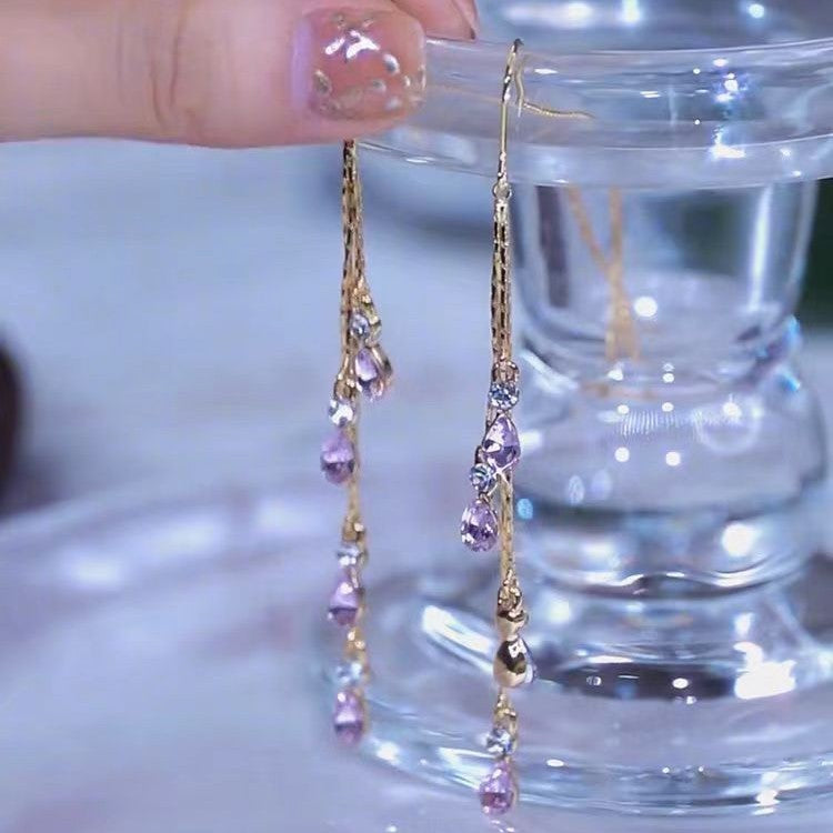 Close-up of purple crystal tassel ear line earrings with gold finish, held by hand