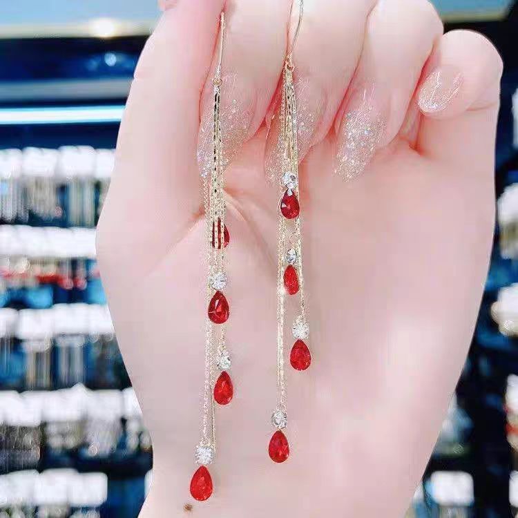 Red crystal tassel ear line earrings with gold finish, held in hand